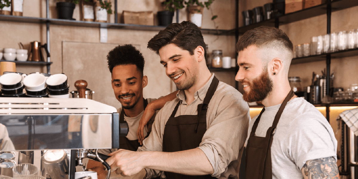 Three baristas smiling, watching one make a drink