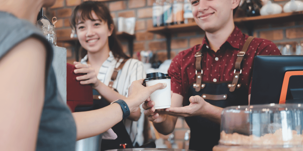 Smiling baristas handing a drink to a customer