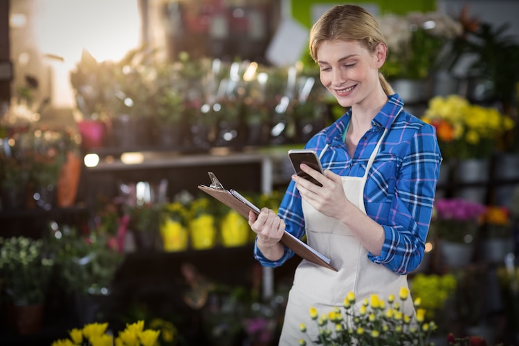 Worker in a garden store smiling, looking at a mobile phone