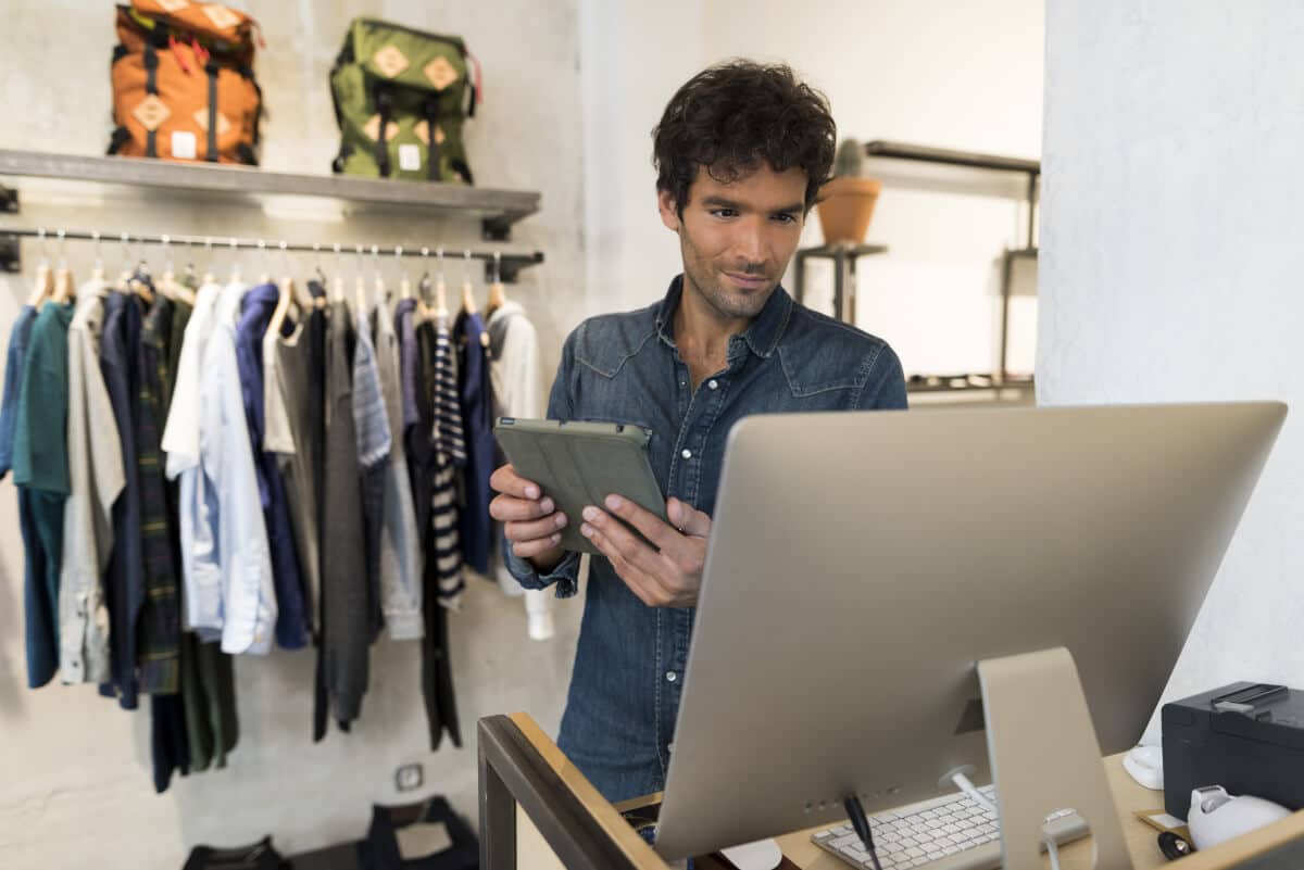 Man in clothing shop looking at mobile device and computer