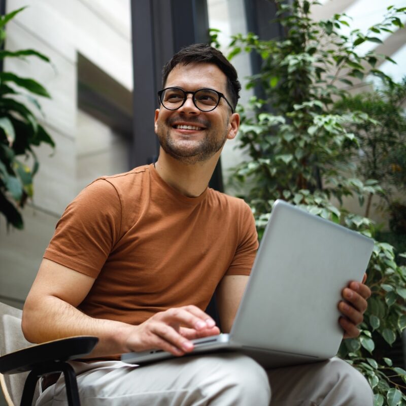 Portrait of a successful young man sitting in the armchair in the modern green building lobby and working on his laptop.